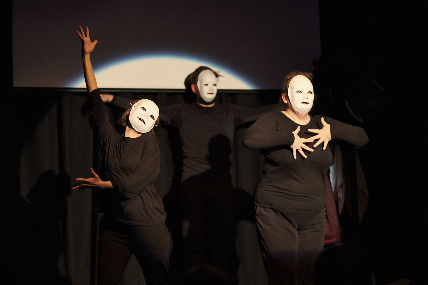 Three black-clad performers in blank white masks in 'Mayhem at the Cabaret Voltaire'